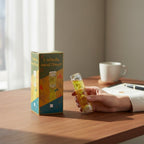 The Witches' Quest 1-minute yellow liquid sand timer held in hand next to its decorative gift box on a wooden desk.
